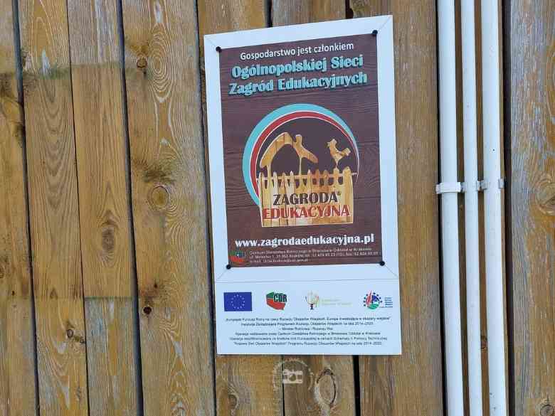 Zagroda Edukacyjna, deski ściany budynku, plakat informacyjny, kable elektryczne w białej izolacji