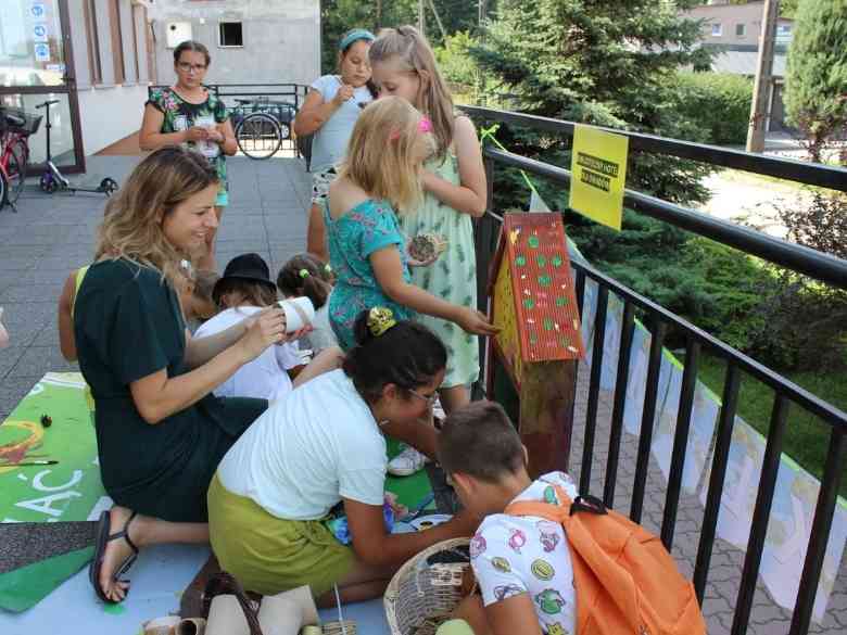 Taras biblioteczny, barierka, Hotel dla owadów, trawa, rower, drzwi, drzewka, dzieci, rower, niebo