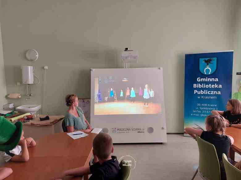 Sala konferencyjna biblioteki, magiczna ściana, stoły, dzieci, baner biblioteczny