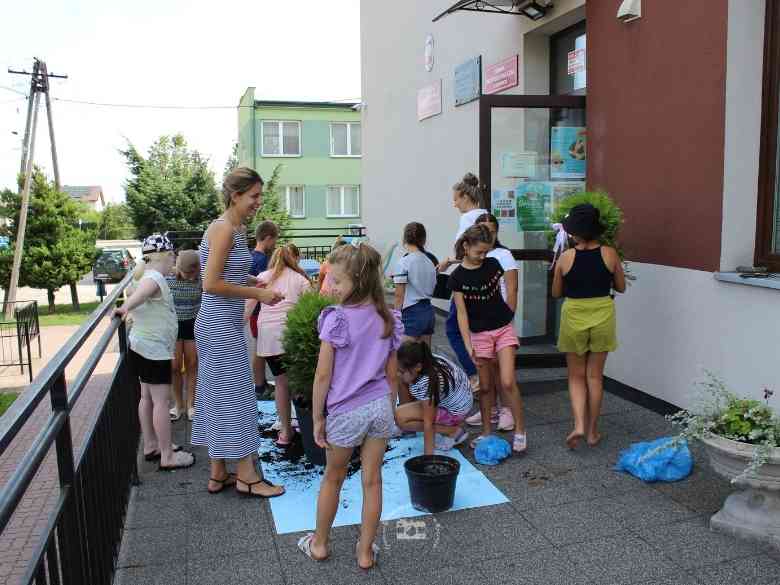 Opiekuni i uczestnicy zajęć sadzący sadzonki przed biblioteką